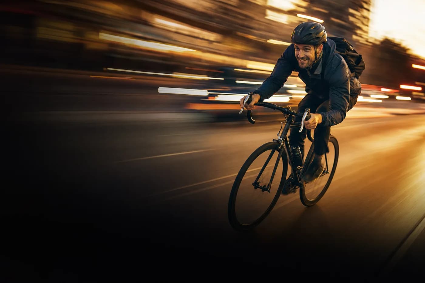 Rennradfahrer lehnt sich in voller Fahrt in die Kurve, Lichter der Stadt ziehen als Streifen vorbei