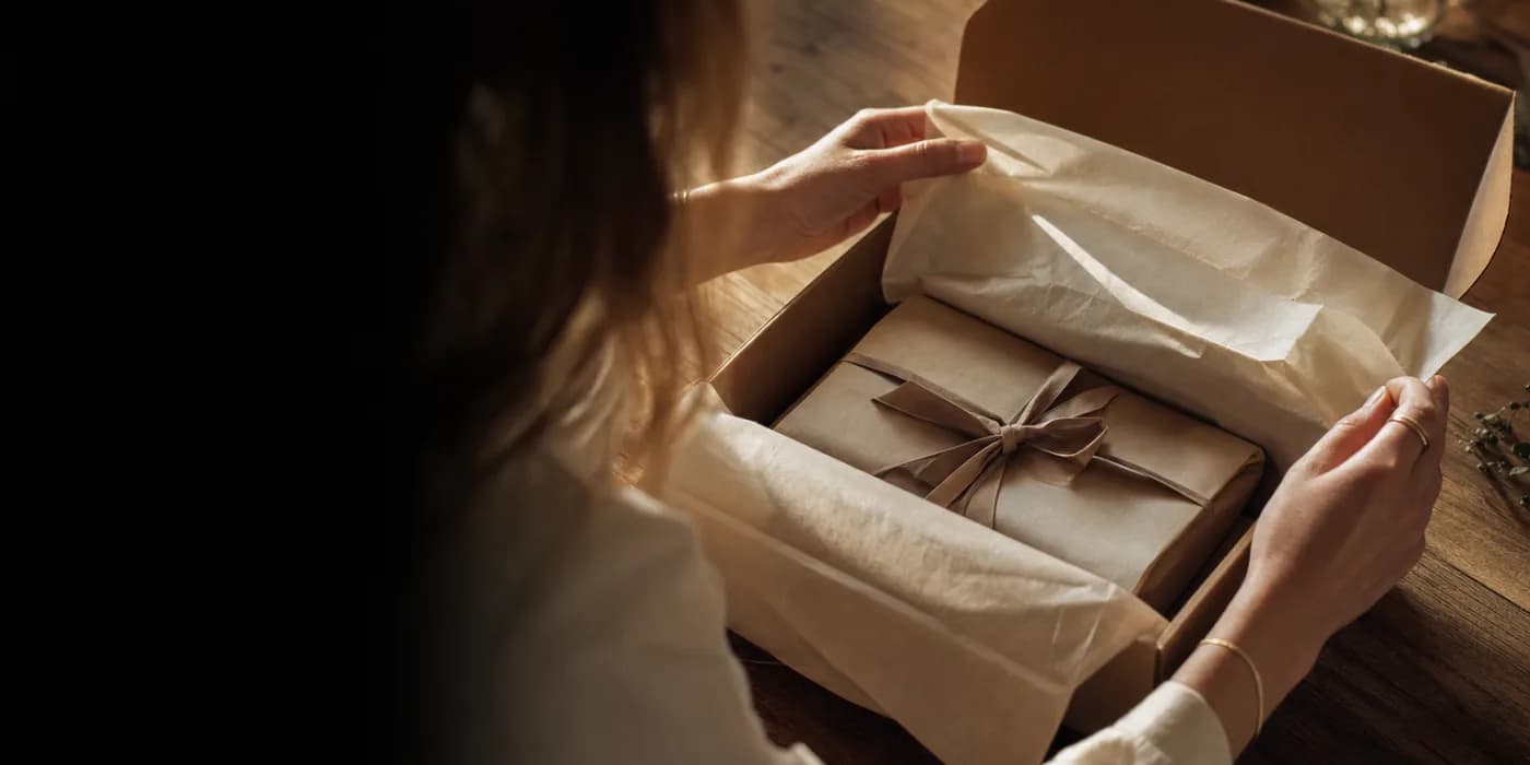 Hände öffnen ein hochwertig verpacktes Paket, Seidenpapier verwischt in warmem Licht